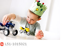 Boy with a crown in his birthday playing with cars on a table