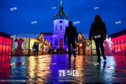 Visitors walk the grounds of the Christmas market in the rain in front of Charlottenburg Palace, which is illuminated in various colours, in Berlin