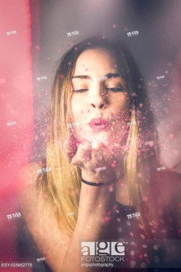Creative pink abstract portrait on the face of a beautiful woman blowing a burst of magic glitter at valentine's day party celebration.