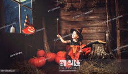 Halloween. little witch child conjures with book of spells, magic wand and pumpkins